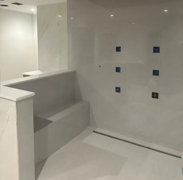 A bathroom with a bench and a shower with blue tiles on the wall.