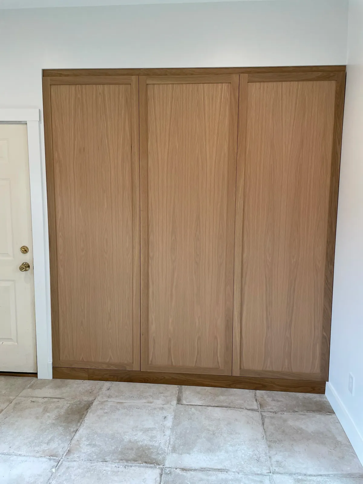 Wooden sliding closet doors in a room with tiled floor and white walls.