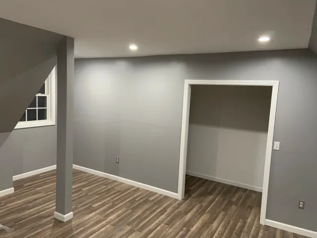 Empty room with gray walls, wooden flooring, a window, and a small closet or alcove.