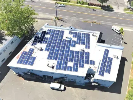 Aerial view of a building roof covered with blue solar panels beside a street and parked cars