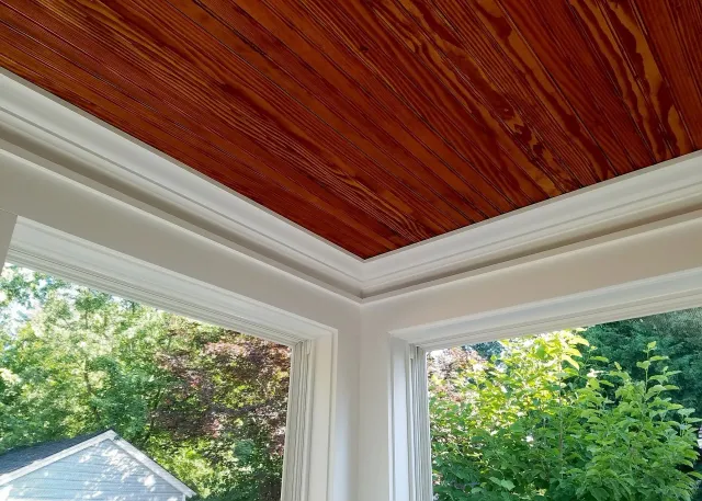 A room with a wooden ceiling and a window with trees in the background.