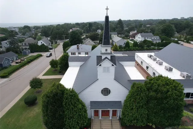 Aerial view of a white church with a tall steeple in a suburban neighborhood.
