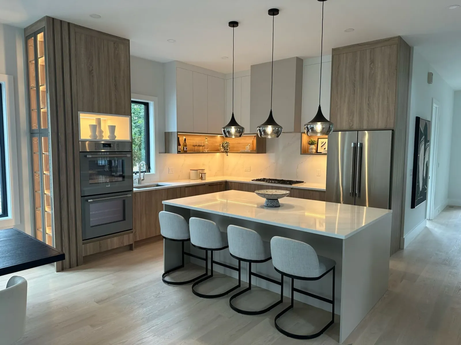 Modern kitchen with light wood cabinetry, a white island with beige bar stools, stainless steel appliances, and pendant lighting.