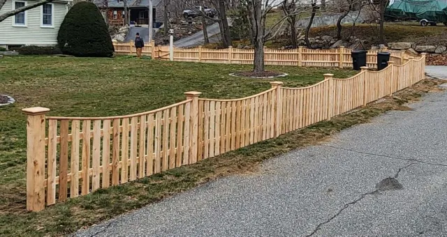 A wooden fence is sitting on the side of a gravel road.