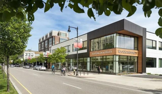 Modern corner storefront on a tree-lined city street with large windows and pedestrians nearby