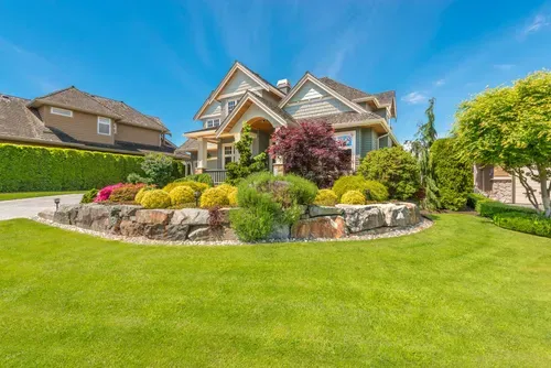 Luxury home with landscaped front yard, stone garden beds, and bright green lawn under a blue sky