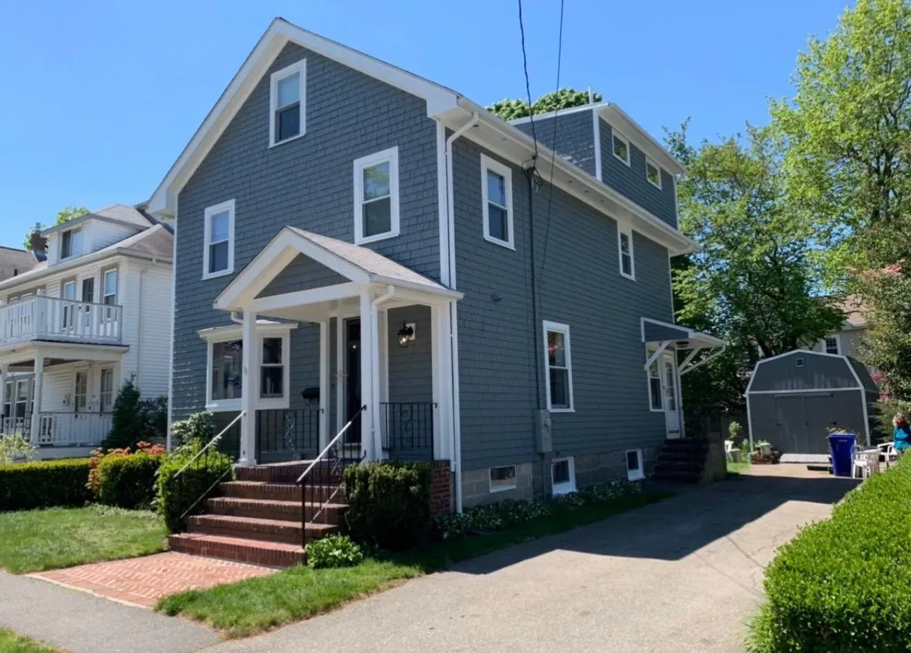 Gray two-story house with white trim, front porch, and driveway on a sunny residential street