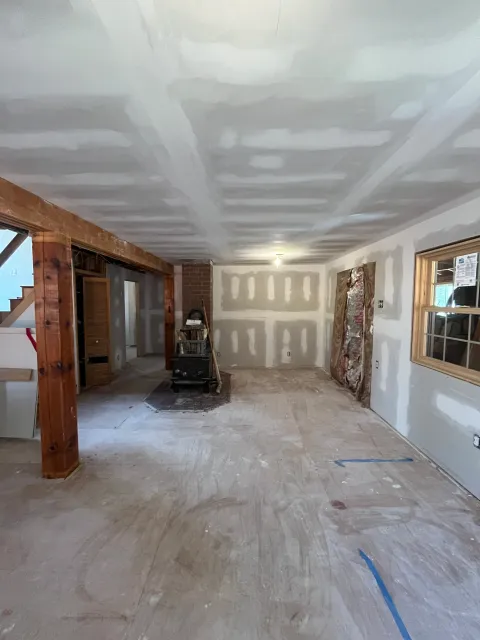 Interior room under construction with drywall ceiling and walls, unfinished flooring, construction tools, and materials.