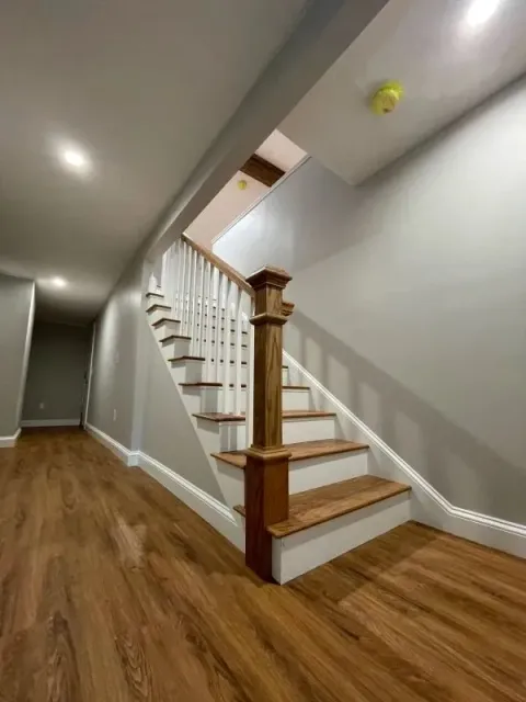 Staircase with white railing and wood treads in a narrow hallway with sloped ceiling and hardwood floor