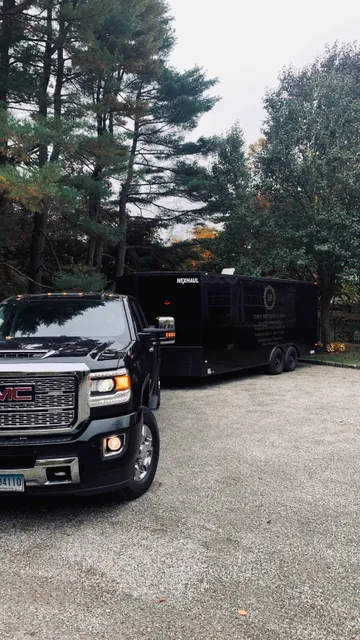 A black truck is parked in a gravel driveway next to a trailer.