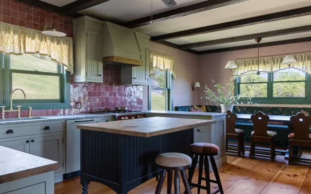 Rustic kitchen with green cabinetry, wooden island, red tile backsplash, and dining nook overlooking garden