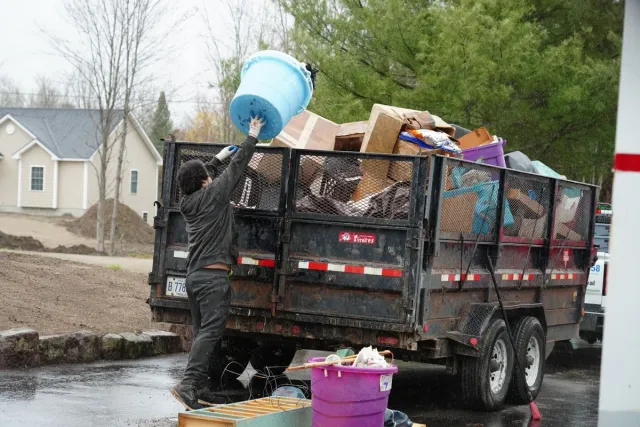A Dump Guy employee emptying a large bucket into a trailer filled with boxes and misc. junk