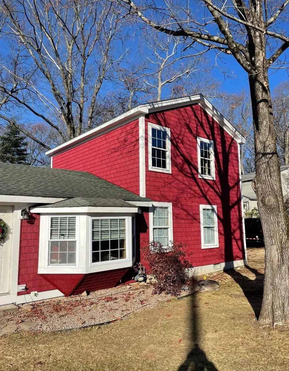 Red house with white trim, green roof, and bare trees under a blue sky.