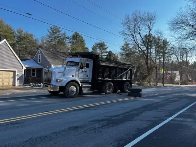 White dump truck with trailer on a suburban road near houses on a sunny day