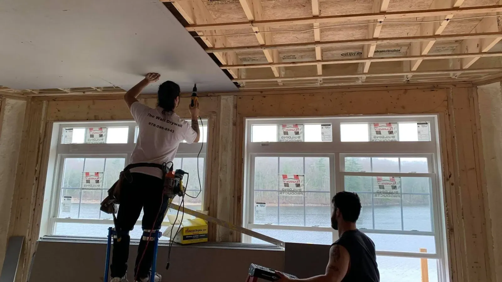 Two men are working on the ceiling of a building.