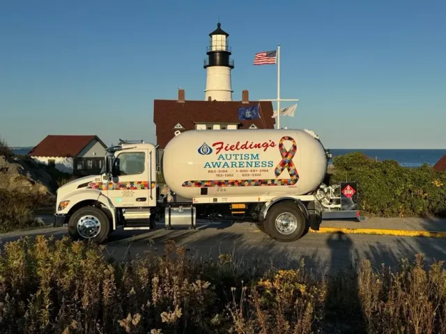 Vintage delivery truck by a lighthouse, with ocean and coastal vegetation in the background