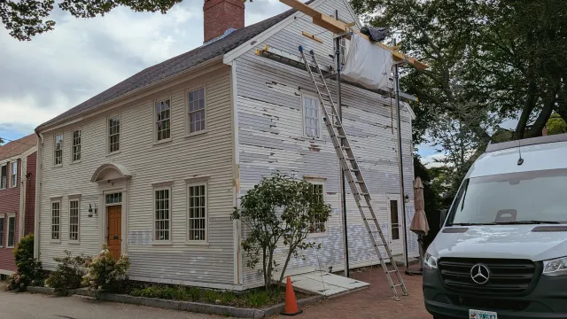 House undergoing renovation with scaffolding on the side, a ladder leaning against it, and a van parked nearby.