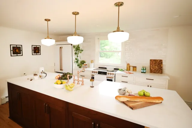 Modern kitchen with white cabinets, window, and brown island, decorated with produce, kitchen utensils, and pendant lighting.