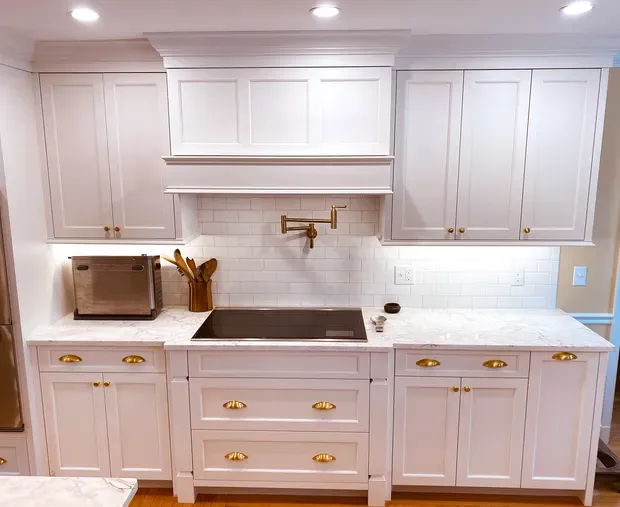 a kitchen with white cabinets, a black stove top, and a pot filler faucet