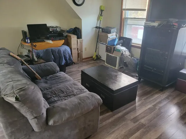 Living room with gray couch, dark coffee table, cluttered desk, and window.