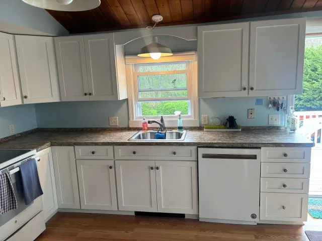 White kitchen cabinets with gray countertops, window over sink.