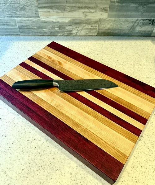 Handmade cutting board of alternating purpleheart and maple stripes with a chef's knife resting on it