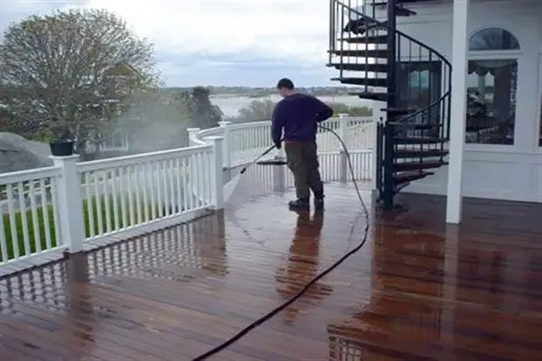 Man power washing a wooden deck with a spiral staircase and water view.