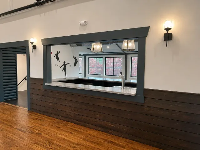 Empty room with wood floor, dark wainscoting, serving window, and wall sconces.