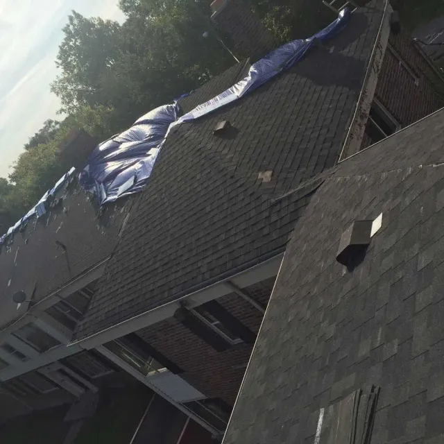 A high-angle view of a shingled roof with a large blue tarp covering a damaged section.