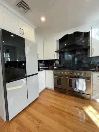 Bright modern kitchen with white cabinets, black appliances, stainless stove, and wood floors