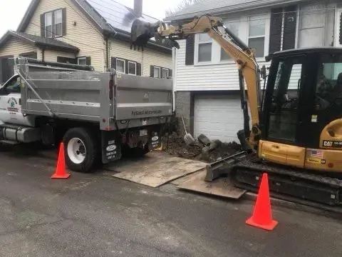 A dump truck and an excavator are parked in front of a house.