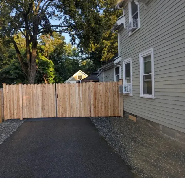 New asphalt driveway leading to a wooden privacy gate beside a gray house