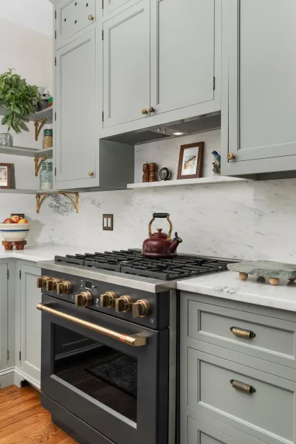 Modern kitchen with sage cabinets, marble backsplash, black range, and copper kettle on the stove