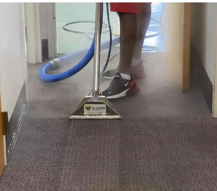 Commercial carpet cleaning in an office hallway with an extraction wand and vacuum hose