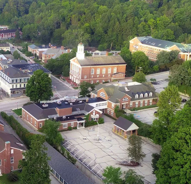 Aerial view of a small town with brick buildings, a schoolyard, and surrounding trees.