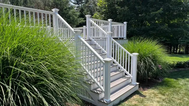 White deck with stairs, surrounded by green grass and bushes in a backyard setting.