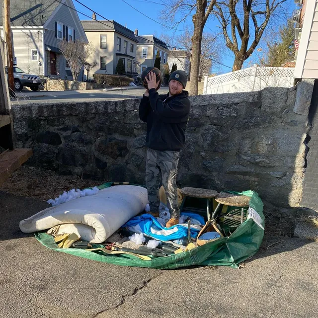 Man holding a ball above a pile of trash, likely cleaning up. Sunny day, urban setting.