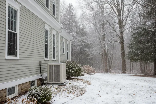 Cold-climate heat pump installed beside a Maine colonial home, surrounded by snow and winter landscaping.