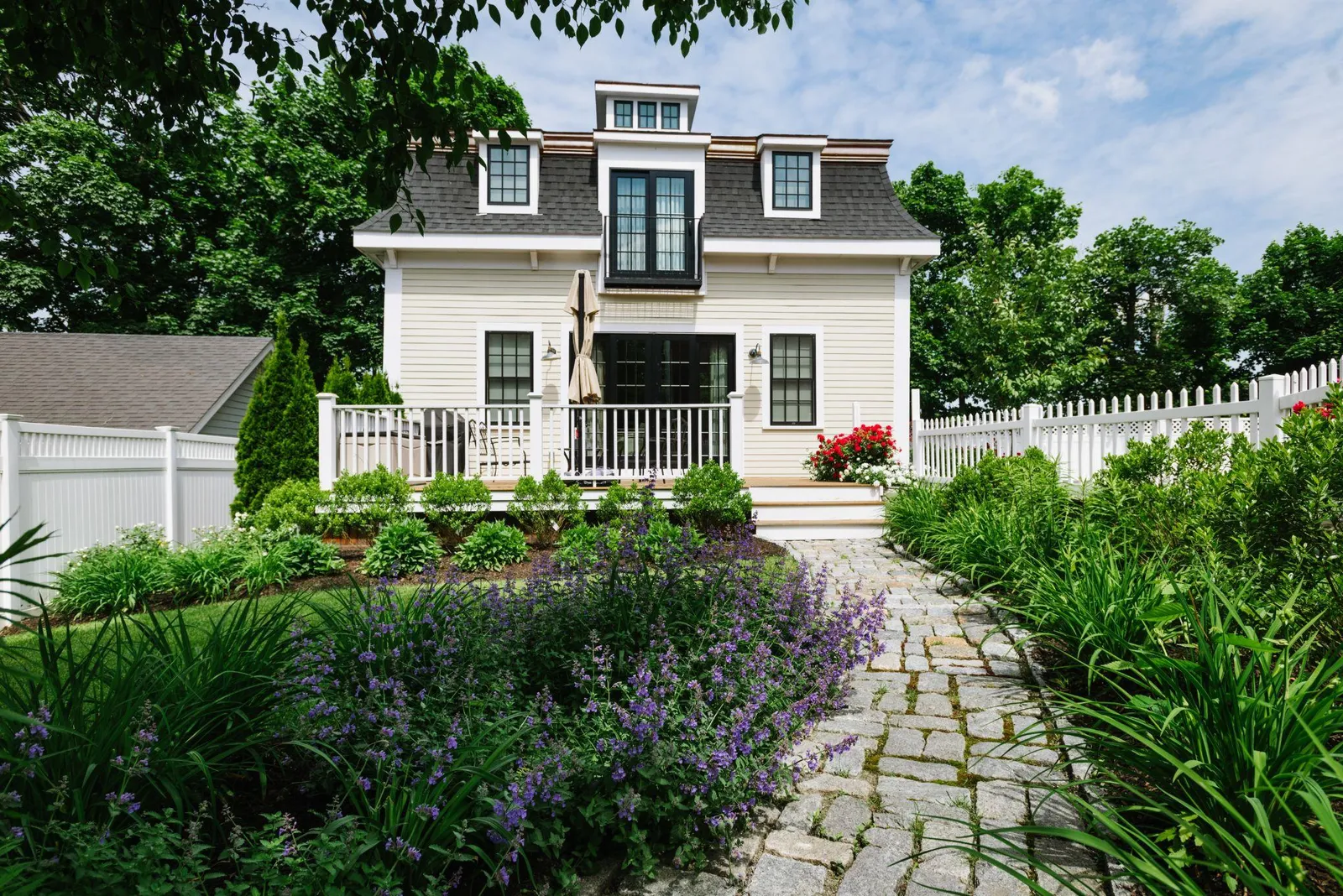 Stone pathway through a lush garden leading to a white cottage-style home.