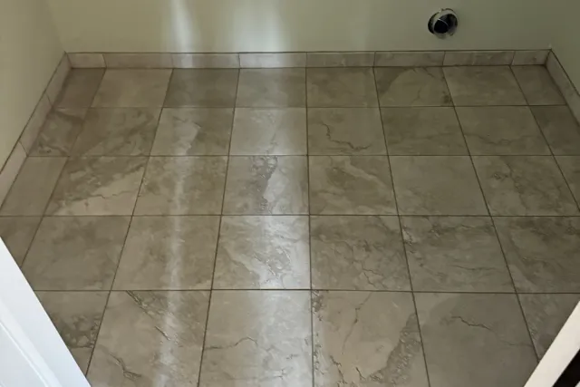 Finished grey marble-look 12×24 porcelain bathroom floor with white baseboard — floor tile installation by Dmtilellc in Plainville, CT