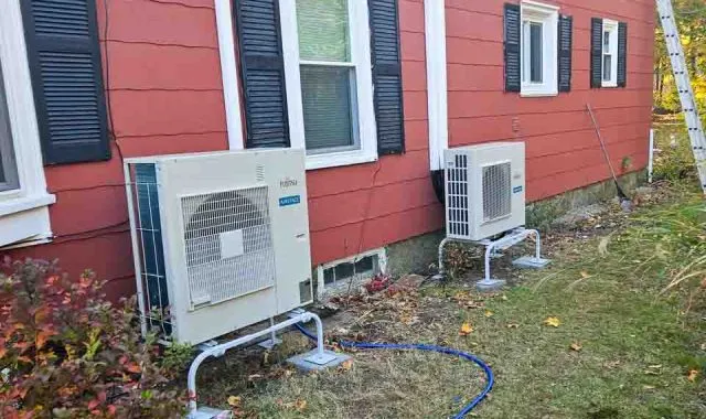 Two Fujitsu heat pump units installed on the exterior of a red house, offering comprehensive heating and cooling capabilities.