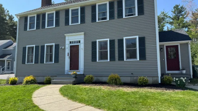 Two-story gray house with dark green shutters and a red front door, with a stone walkway.