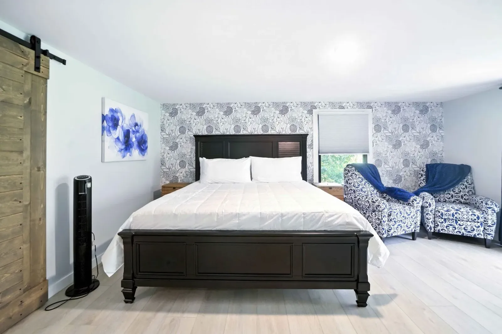 Bright bedroom with a dark bed, floral wallpaper, blue chairs, and a rustic sliding door