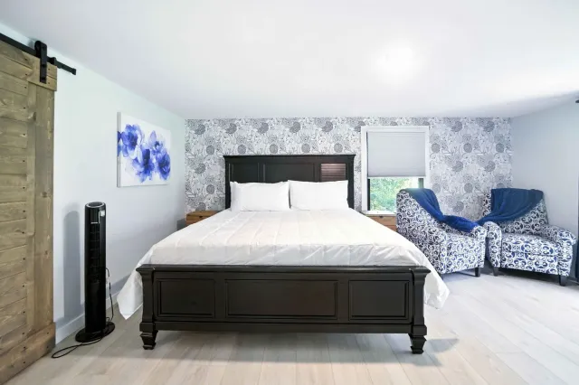 Bright bedroom with a dark bed, floral wallpaper, blue chairs, and a rustic sliding door