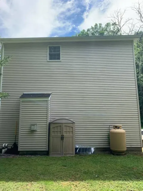 Back of a beige house with a small shed, side door, propane tank, and grassy yard under a blue sky