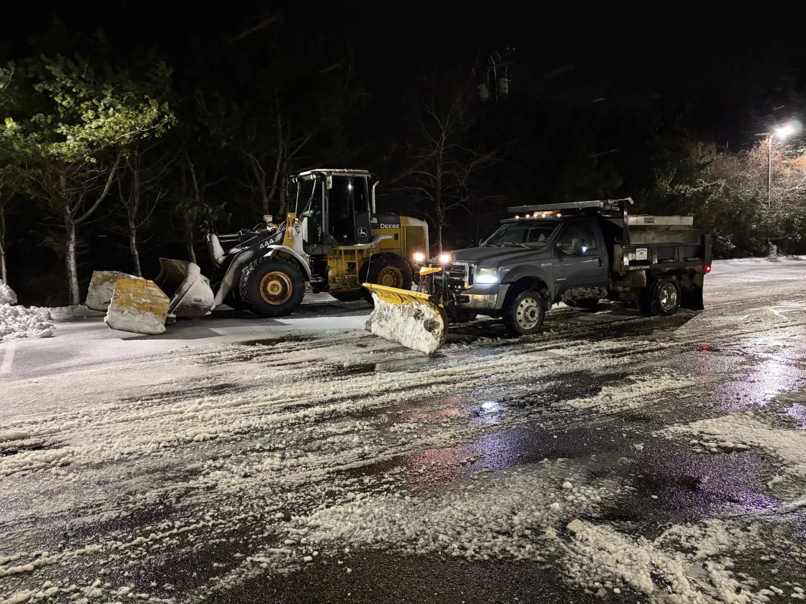 Snowplow and loader clearing a snowy road at night.