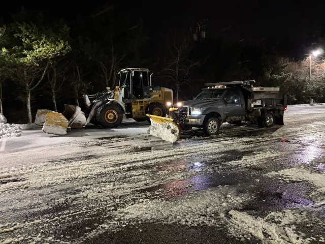 Snowplow and loader clearing a snowy road at night.