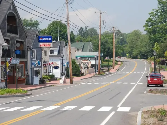 Quiet curving road with a red car, small roadside buildings, and trees on a sunny day