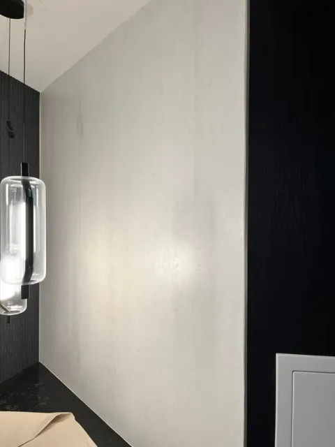A modern interior featuring a textured light grey wall flanked by black panels, illuminated by a cylindrical pendant light.