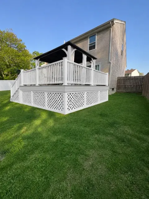 White wooden deck attached to a house, with a lattice base and green lawn in the yard.